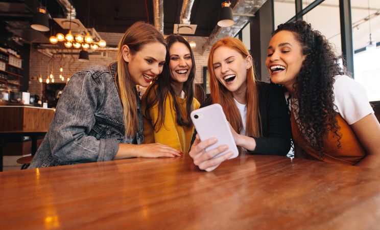 Group of young women sitting in a cafe and looking at the photos on smart phone
