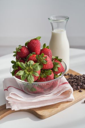 Bowl with fresh strawberries and bottle of milk on wooden choppi