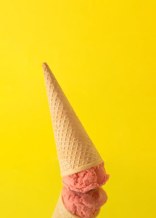 Upside-down cone with pink scoop of ice cream on yellow background