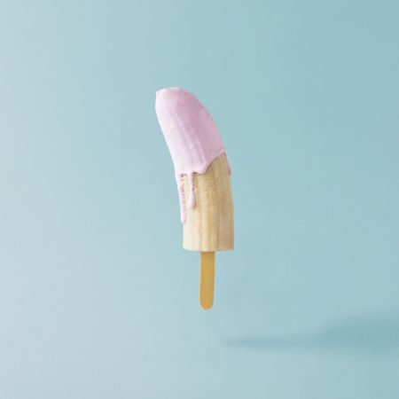 Banana with ice cream stick and pink syrup on pastel blue background