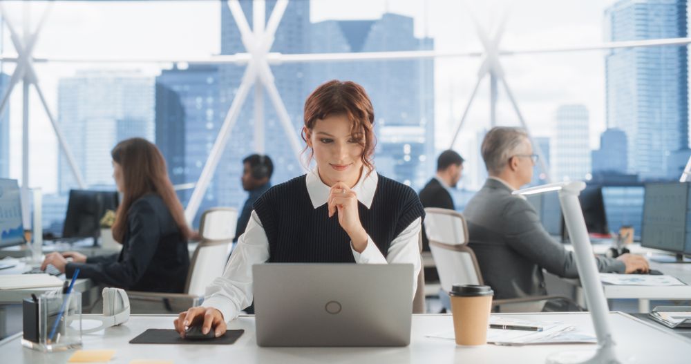 Female Sales Manager Writing Emails To Clients In Workspace With Diverse Colleagues.