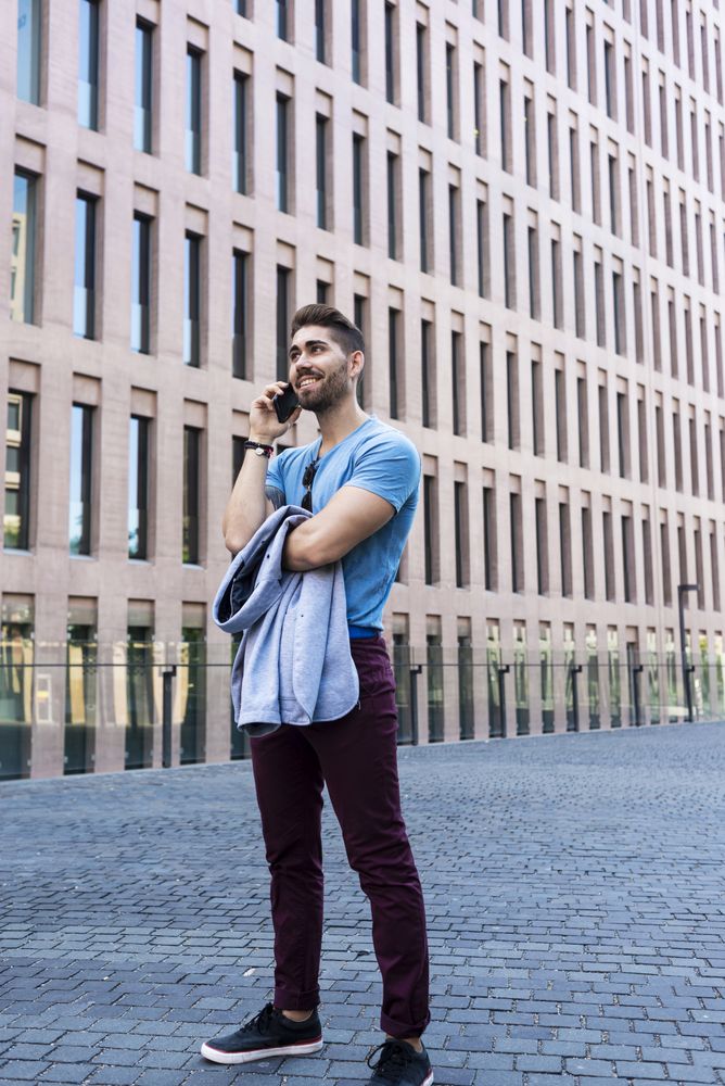 Portrait of cheerful modern businessman speaking by phone and smiling while standing outdoors