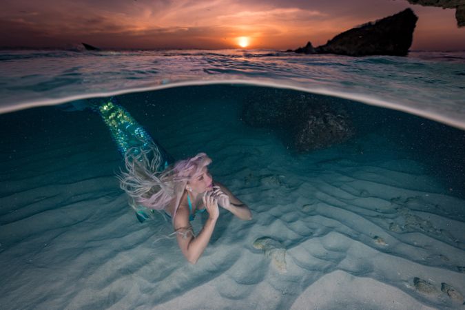 Blond fairytale female mermaid swimming along sea bottom