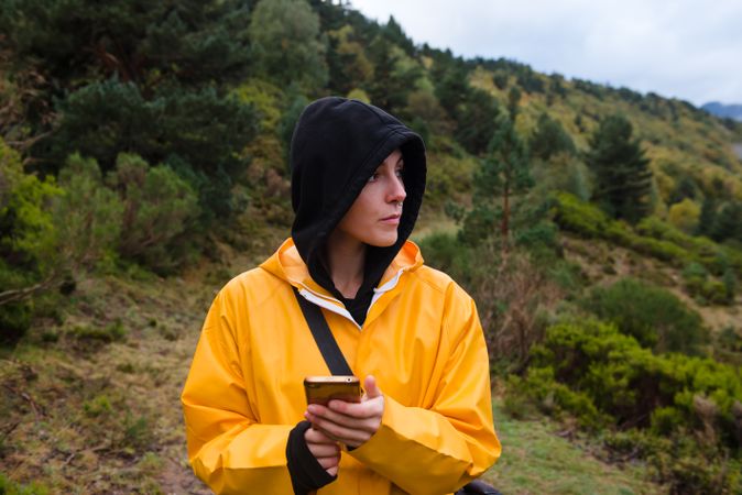 Woman in hoodie and yellow raincoat browsing smartphone