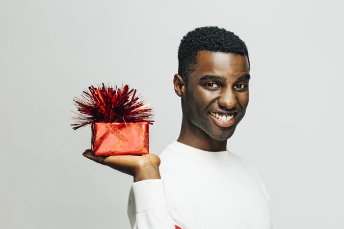 Smiling Black man holding up a present wrapped in red