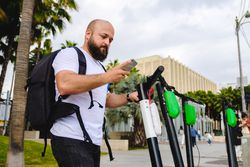 Traveler with backpack browsing smartphone and choosing electronic scooter