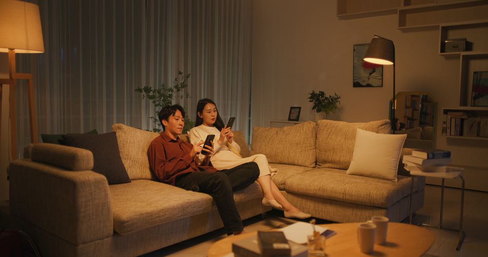 Young South Korean Couple Using Smartphones While Relaxing on a Couch at Home