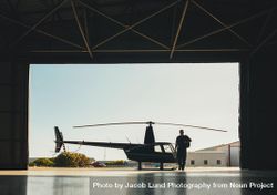 Silhouette of a pilot walking in hangar with a parked helicopter be6yN0