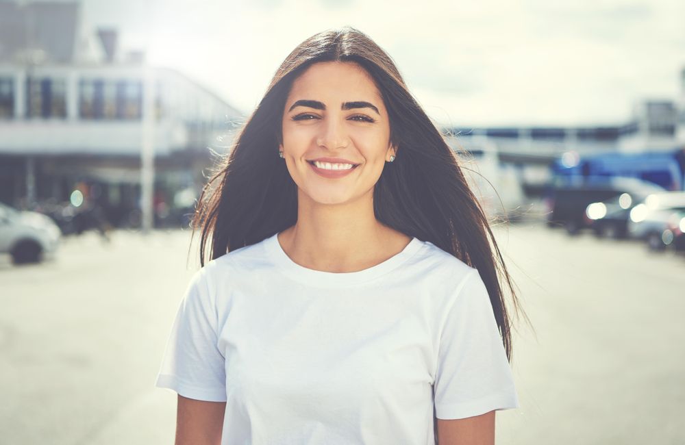 Smiling woman with long straight brown hair outside on street with parked cars