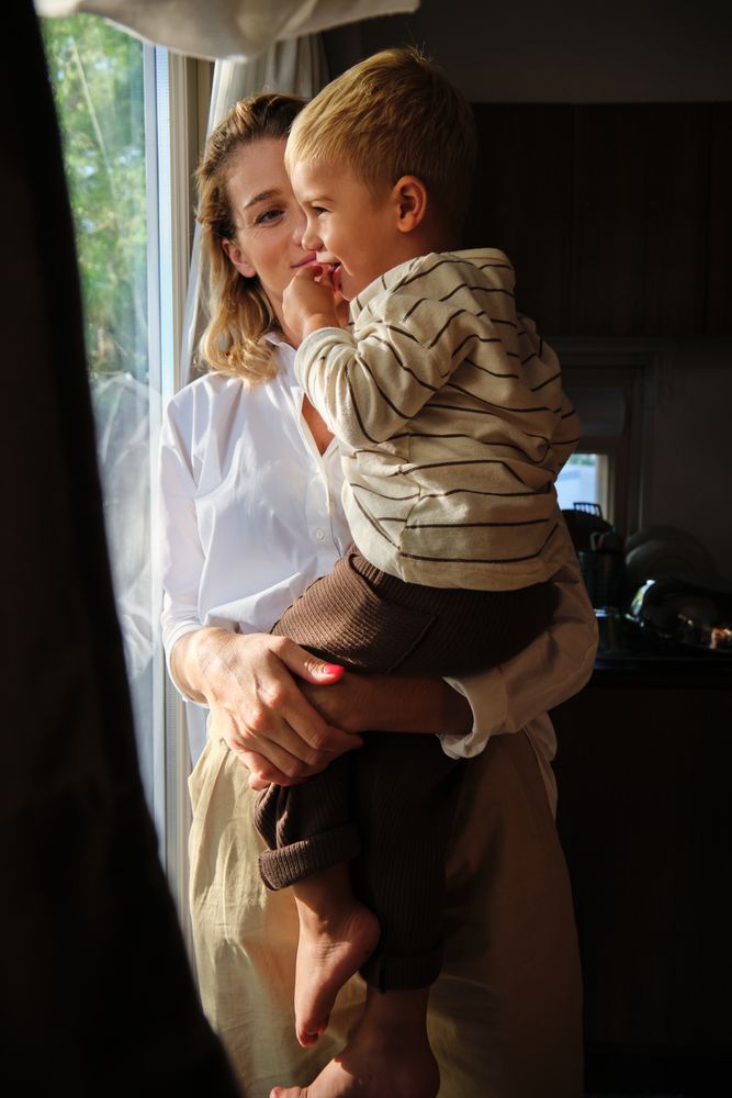 Woman standing near window and holding son in hands