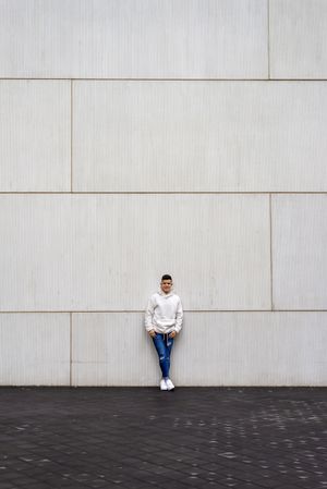 Young man in bright hoodie leaning on wall outside, vertical composition
