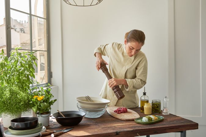 Woman making steak tartare at table in kitchen