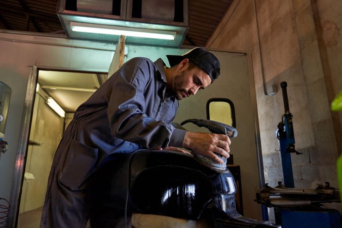 Mechanic polishing motorbike tank in garage