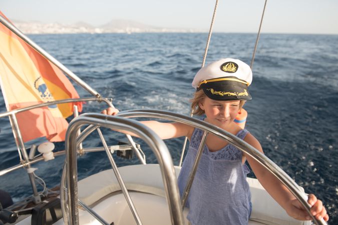 Smiling girl holding steering wheel on yacht on water