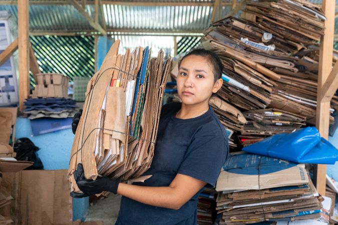 Young Hispanic Woman Holding Heavy Cardboard Stack. Serious Expression