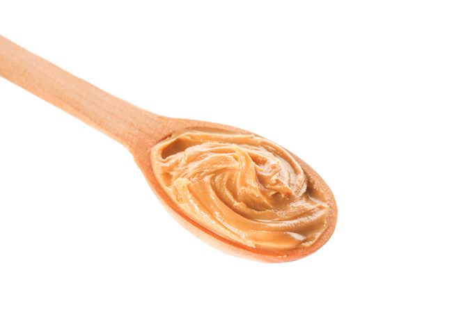Creamy peanut butter in wooden spoon isolated on bright background, closeup. A traditional product of American cuisine