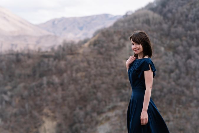 Woman in long blue dress standing near mountainous landform