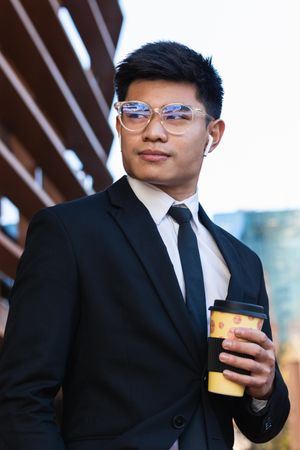 Handsome Asian businessman with takeaway coffee in city