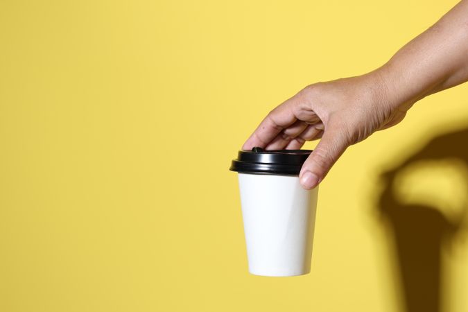 Hand Holding Coffee Papercup on Yellow Background