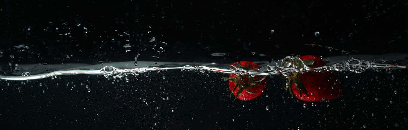 Side view banner of water on dark background with floating strawberries and copy space