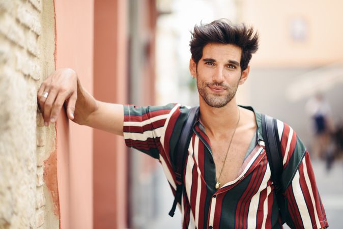 Handsome man with dark hair wearing casual clothes leaning on wall outdoors