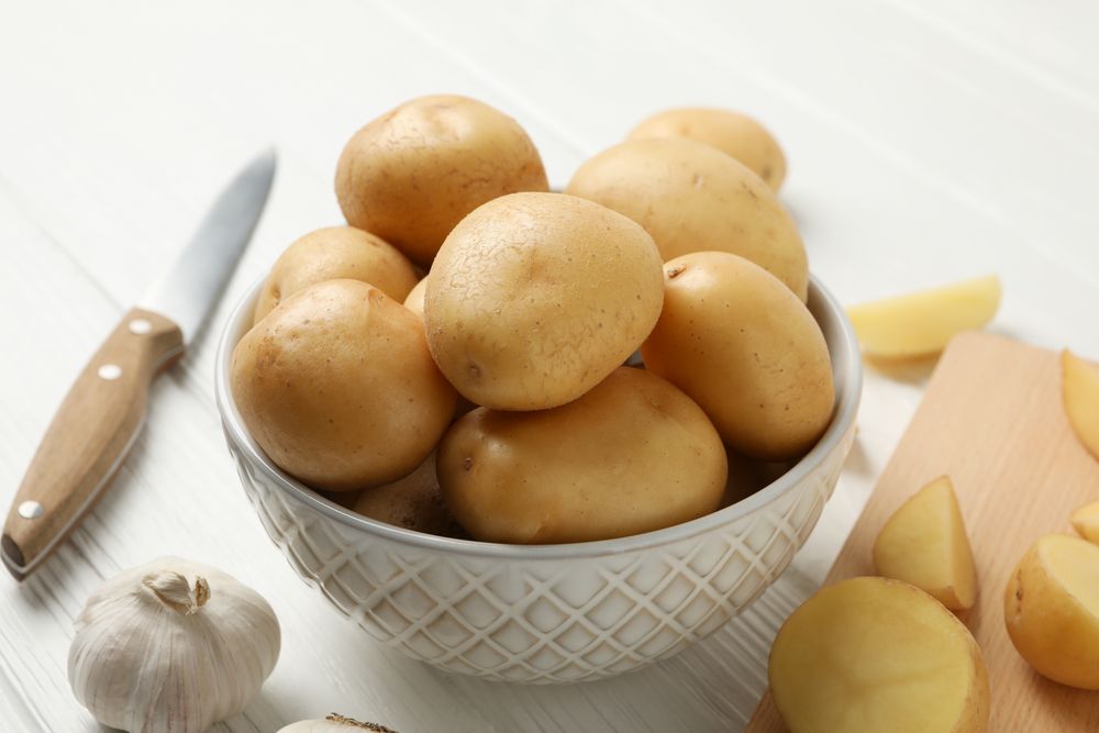 Bowl full of potatoes on kitchen counter with garlic and knife