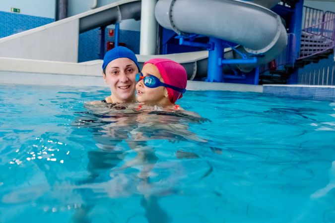 Cheerful girl swimming in pool with mother
