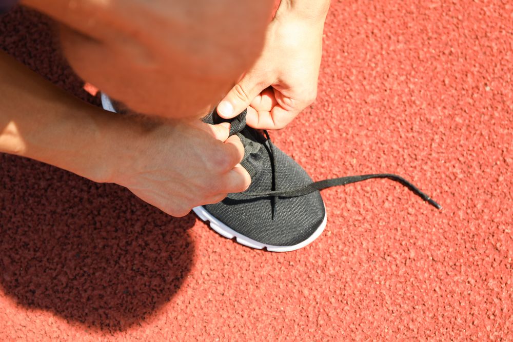 Man tying shoelaces on red athletic running track, close up