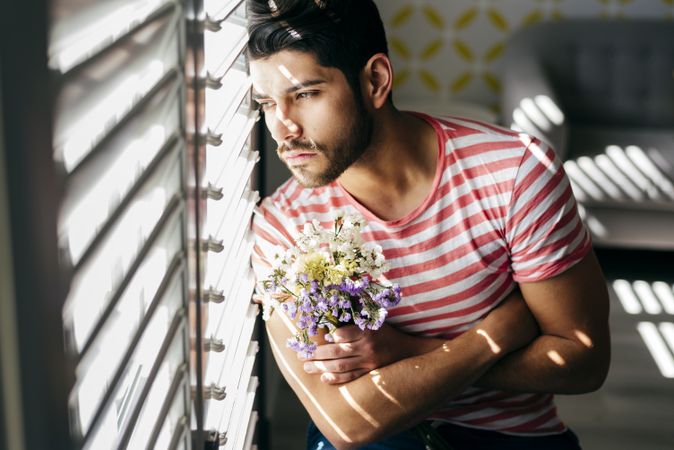 Young sad man with flowers looking out window