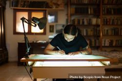 Tattooed woman sketching on a light table in a studio bGGjAb