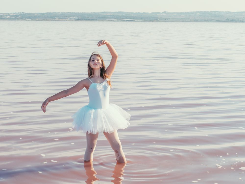 Ballerina in swimsuit with tutu performing classical position in water
