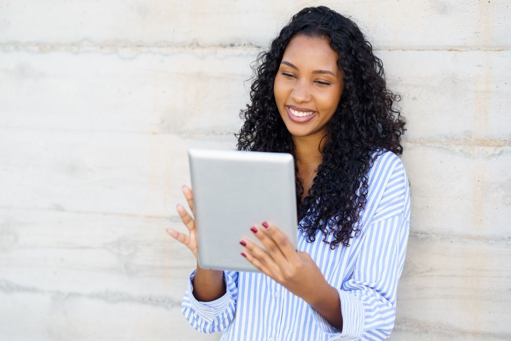 A Young Woman is Engaged with a Digital Tablet While Outdoors, Dressed in Casual Attire