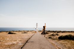 Happy lovers jumping with arms raised on path to lighthouse