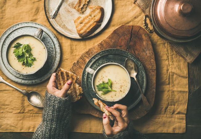 Woman breaking toast over cup of celery soup