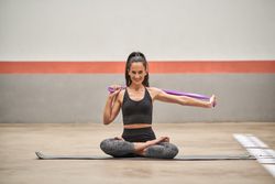 Smiling sportswoman stretching arms with elastic band i