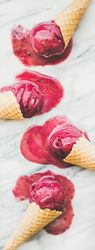 Four cones of dark berry ice cream melting on marble slab, vertical composition
