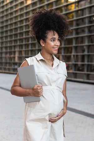 Smiling Black woman with laptop coming out of office building