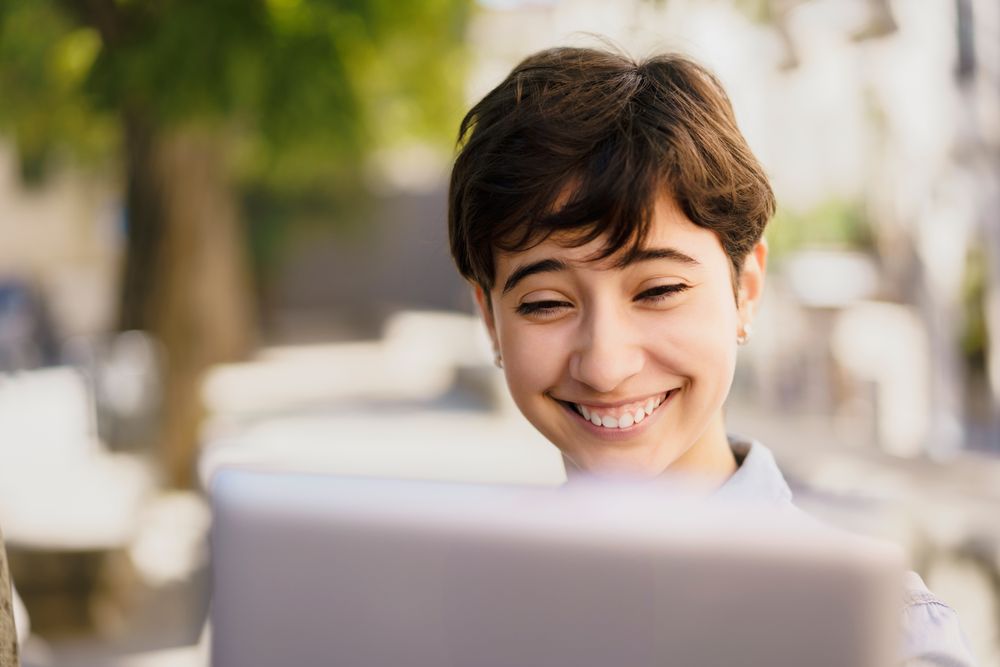 A Happy Young Individual Fully Engaged in Performing Remote Work on a Laptop Outdoors