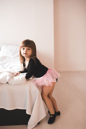 Young girl in pink tutu standing beside light linen bed