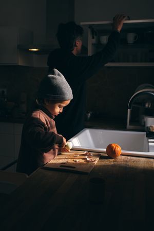 Curious child peeling mandarins at table near anonymous dad