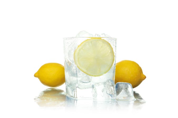 Rocks glass full of ice with lemon slice, surrounded by whole lemons