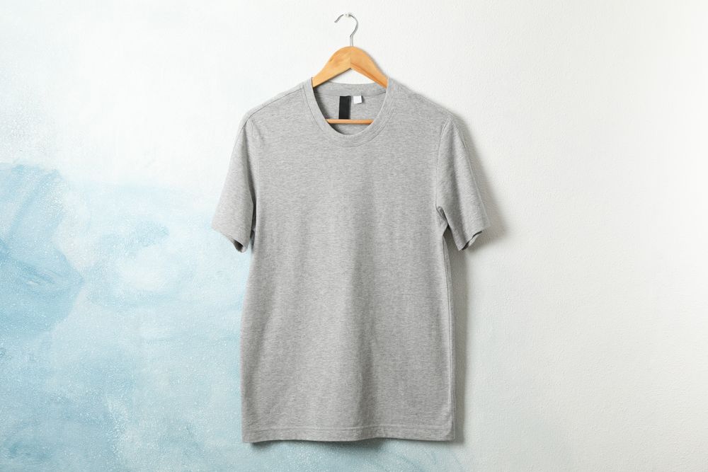 Hanger with blank gray t-shirt on blue background, space for text
