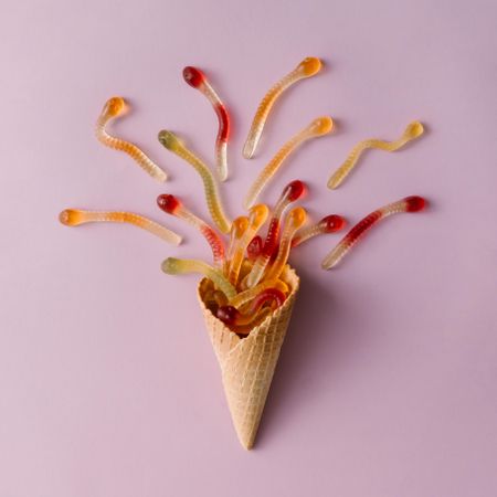 Waffle cone with gummy worms on pastel purple background