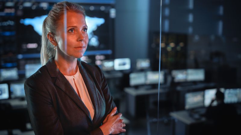 Focused Professional Woman in Control Room, Analyzing Data on Digital Screens.