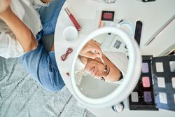 Crop woman doing eyes makeup with brush sitting on floor