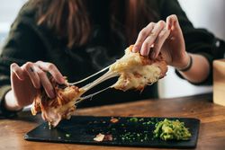 Woman pulling apart croissant sandwich with melted cheese