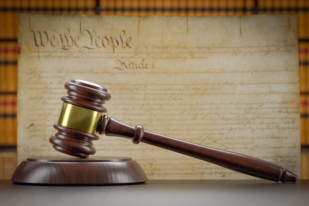 United States Constitution On Wall with Gavel Resting on Table in Front.