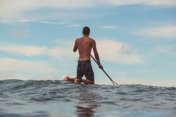Man with paddle on surf board waving on water