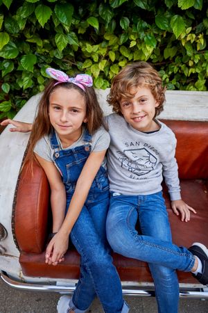 Cute preteen girl in headband sitting on sofa with smiling boy