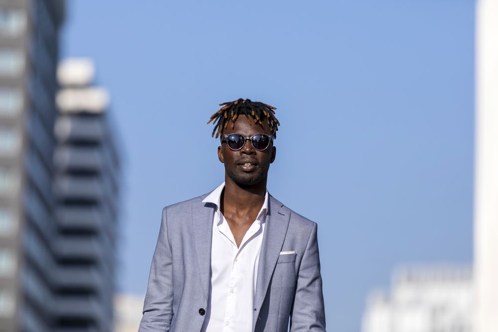 Front view of Black man in elegant suit walking on the street against a blue sky